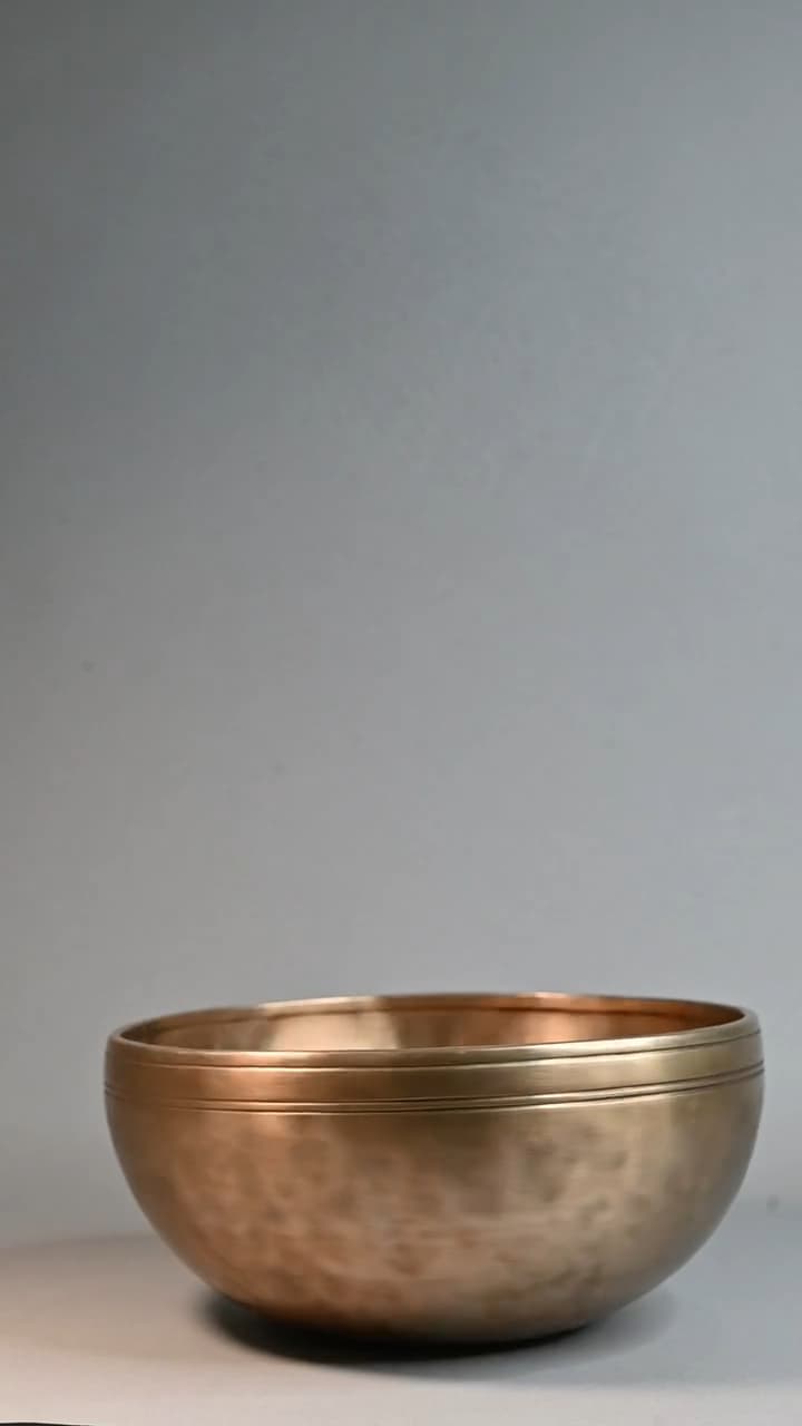 A single bronze singing bowl on a seamless grey studio backdrop, plain flank facing the camera