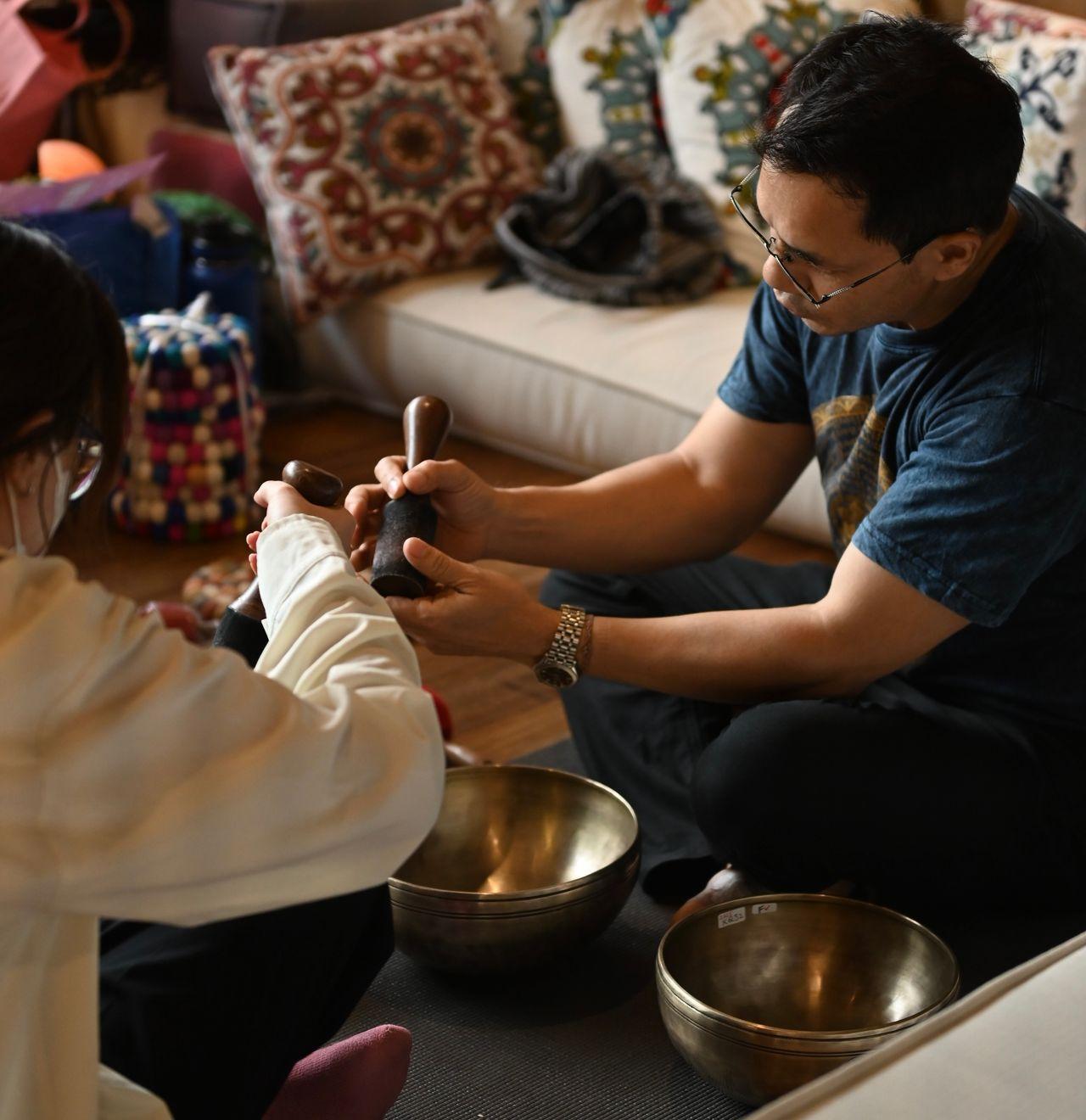 Hands exchanging wooden and felt mallets over two bowls