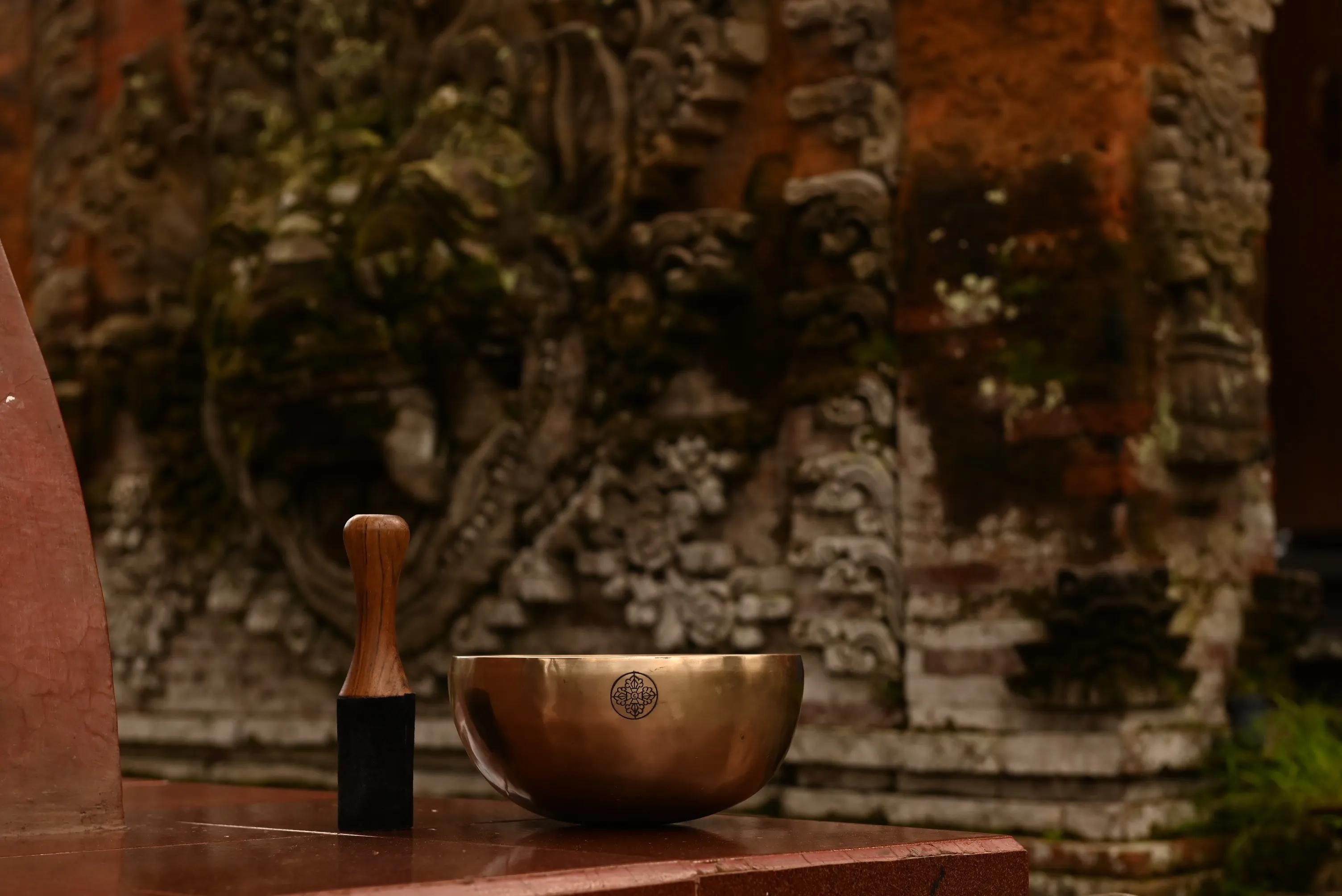 A hand-hammered singing bowl stamped with Santa's maker's mark, standing on a wooden shelf among other bowls