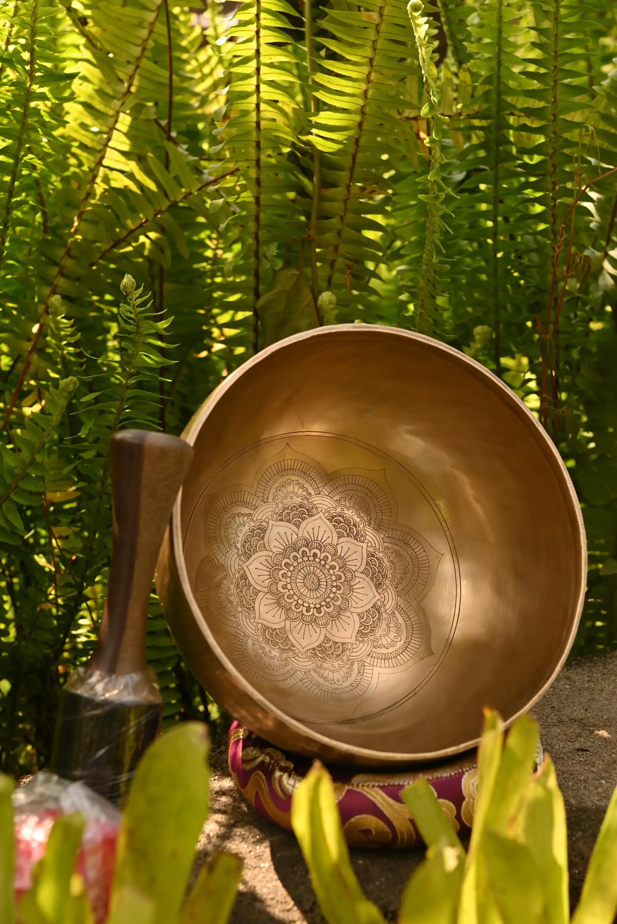 A bronze singing bowl engraved with a lotus mandala, beside its wooden mallet before a weathered carved temple wall